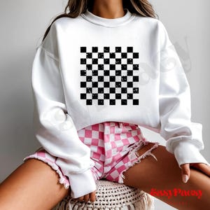 Puede incluir: Sudadera blanca con un gráfico de patrón de cuadros blanco y negro. La modelo lleva pantalones cortos de cuadros rosa y blanco.