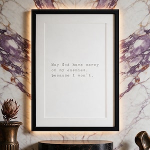 Framed typographic dark humour print on a violet-veined marble wall above a dark marble plinth with bronze planter.