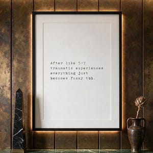 Framed typographic dark humour print on a patinated bronze panelled wall above a green marble console.