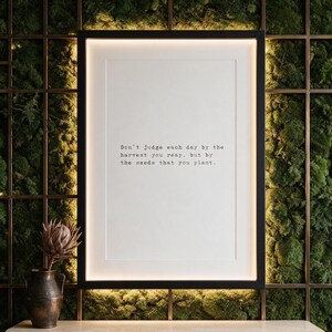 Framed black and white typographic growth print on a full moss wall above a travertine console.