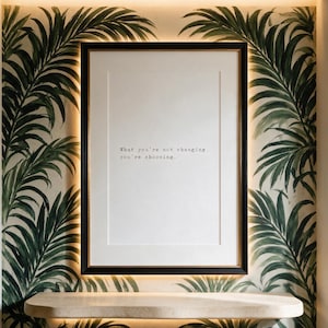 Black and white discipline typography print in a dark gilt-lined frame on a hand-painted palm mural wall, hallway decor above a pale travertine shelf, a considered gift for a home office.