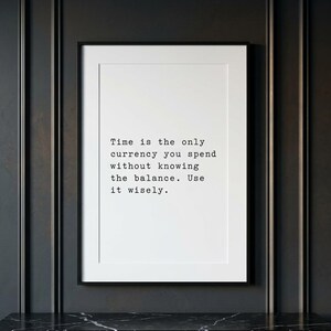 May include: A rectangular framed wall art piece featuring a white background with black typewriter-style text that reads: Time is the only currency you spend without knowing the balance. Use it wisely. The frame is thin and black.