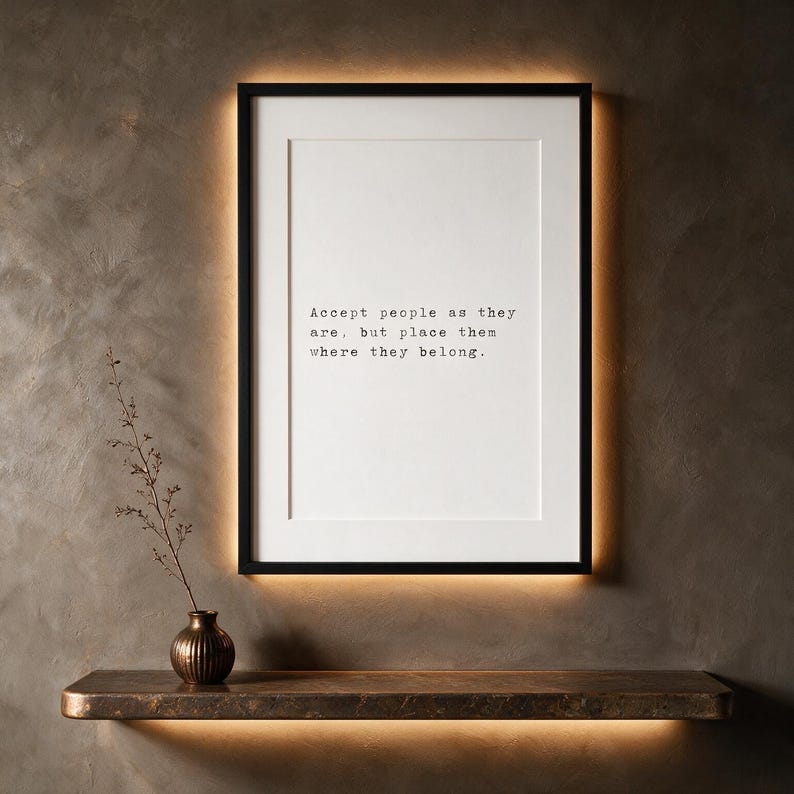 Framed black and white typographic philosophy print on a warm taupe limewashed wall above a floating travertine console.
