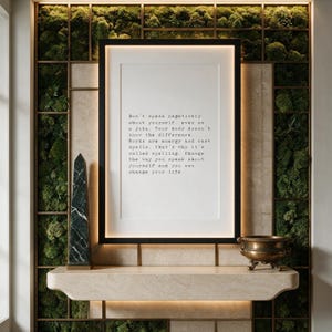 Framed typographic self talk print on a preserved moss and bronze grid wall above a pale travertine console.