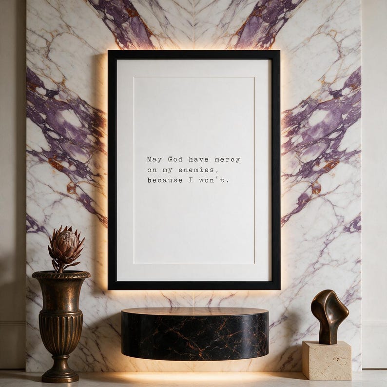 Framed typographic dark humour print on a violet-veined marble wall above a dark marble plinth with bronze planter.