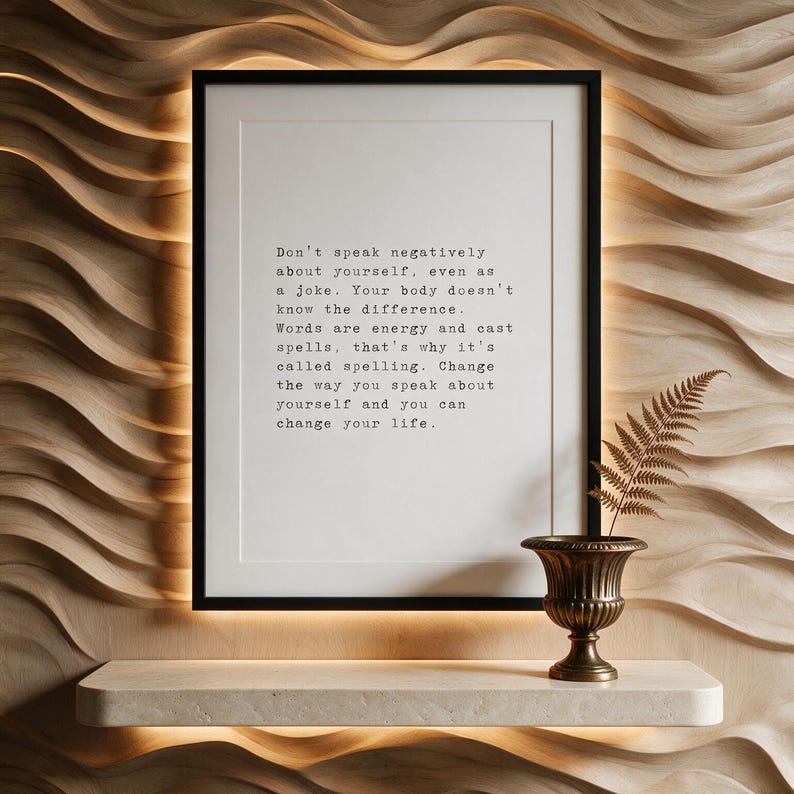 Framed black and white typographic self talk print on a carved pale oak wave wall above a travertine console.