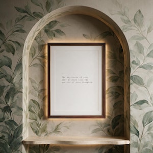Framed black and white stoic quote print in a dark walnut frame within a plastered arch niche hand painted with botanical leaves, above a pale stone shelf, a thoughtful gift for a reader or philosophy lover.