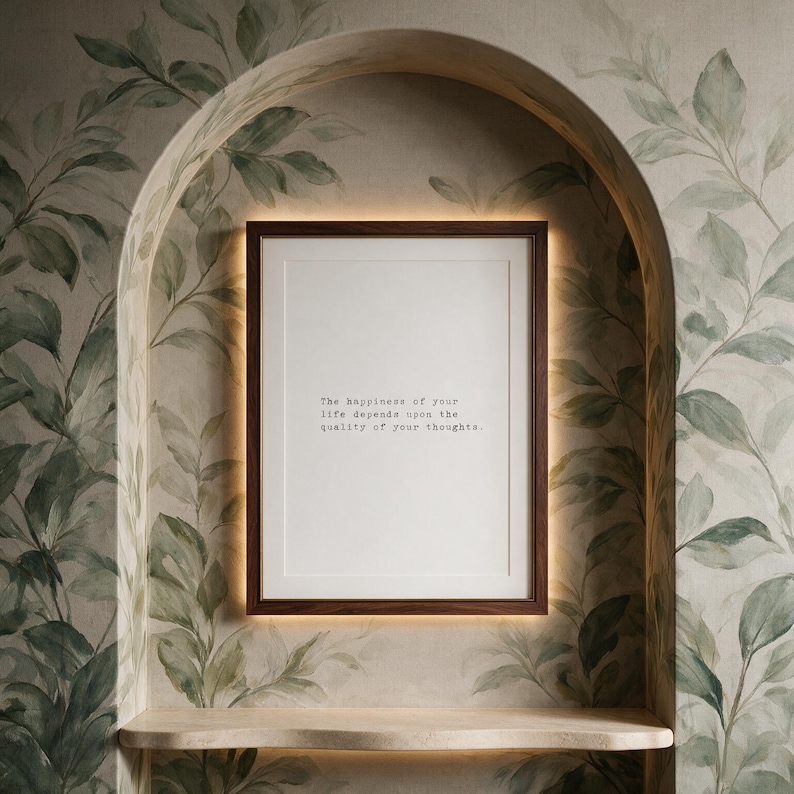 Framed black and white stoic quote print in a dark walnut frame within a plastered arch niche hand painted with botanical leaves, above a pale stone shelf, a thoughtful gift for a reader or philosophy lover.