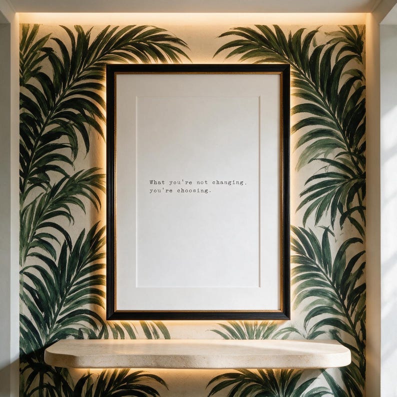 Black and white discipline typography print in a dark gilt-lined frame on a hand-painted palm mural wall, hallway decor above a pale travertine shelf, a considered gift for a home office.