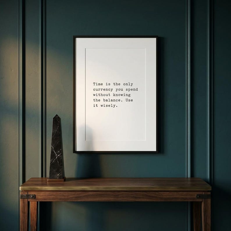 May include: A framed white wall art print featuring black typewriter-style text that reads: Time is the only currency you spend without knowing the balance. Use it wisely. The print is displayed in a thin black frame with a white mat border.