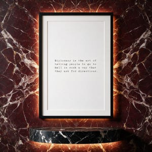 Typography quote print in a black frame set against deep claret book-matched marble with a backlit niche.