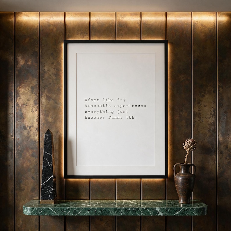Framed typographic dark humour print on a patinated bronze panelled wall above a green marble console.