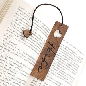 Könnte beinhalten: Ein Holz-Lesezeichen mit einem herzförmigen Ausschnitt und dem Wort "Heike" eingraviert. Das Lesezeichen ist braun und hat ein schwarzes Gummiband.