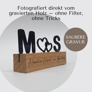 May include: A wooden block with the letters "M❤️S" in black, with a heart symbol between the letters. The block has the phrase "Hand in Hand - ein lebenlang" engraved on it. The text "SAUBERE GRAVUR" is also visible.