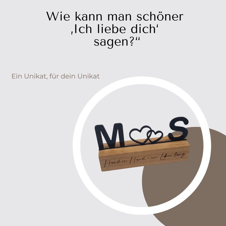 May include: Wooden block with black letters spelling "M S" and two intertwined hearts. The block has the text "Hand in Hand - ein Leben lang" engraved on it. The image also includes the text "Wie kann man sch&ouml;ner 'Ich liebe dich' sagen?" and "Ein Unikat, f&uuml;r dein Unikat".