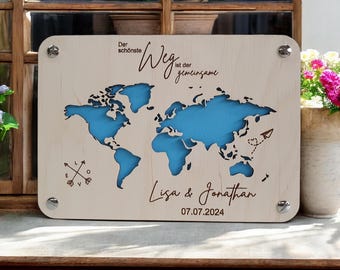 May include: A wooden world map with a blue outline of the continents. The text "The most beautiful way is the shared one" is written in German. The names "Lisa & Jonathan" and the date "07.07.2024" are written below the map.