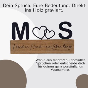 May include: A wooden block with the letters "M" and "S" in black, with two intertwined heart shapes in the middle. The block has the phrase "Hand in Hand - ein (eben lang)" engraved on it. The image also contains German text.