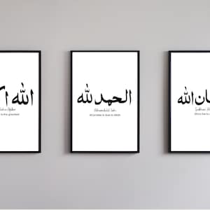 Puede incluir: Tres impresiones enmarcadas en negro con fondos blancos y caligrafía árabe negra. El texto de las impresiones se traduce como "Allah es el más grande", "Toda alabanza es debida a Allah" y "Gloria a Allah".