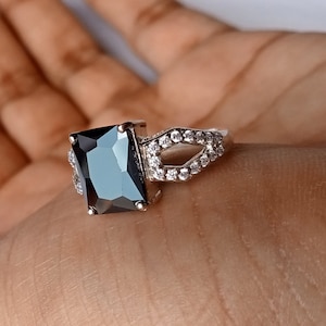 May include: A silver ring with a large black square-shaped gemstone and smaller white gemstones on the band.
