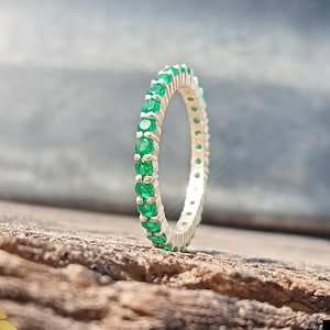 Puede incluir: Un anillo de banda de plata con una fila de piedras preciosas de color verde esmeralda.