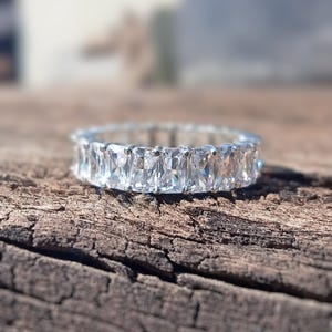 May include: A silver ring with a row of clear, rectangular-shaped stones.