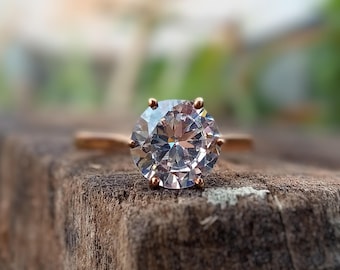 May include: A gold ring with a large, clear, round gemstone. The ring is sitting on a piece of rough, brown wood.