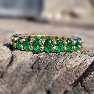 Op de afbeelding: Een gouden ring met een rij smaragdgroene edelstenen.