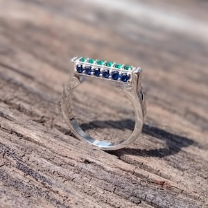 Könnte beinhalten: Ein silberner Ring mit einem rechteckigen Band, das mit abwechselnd grünen und blauen Edelsteinen besetzt ist.