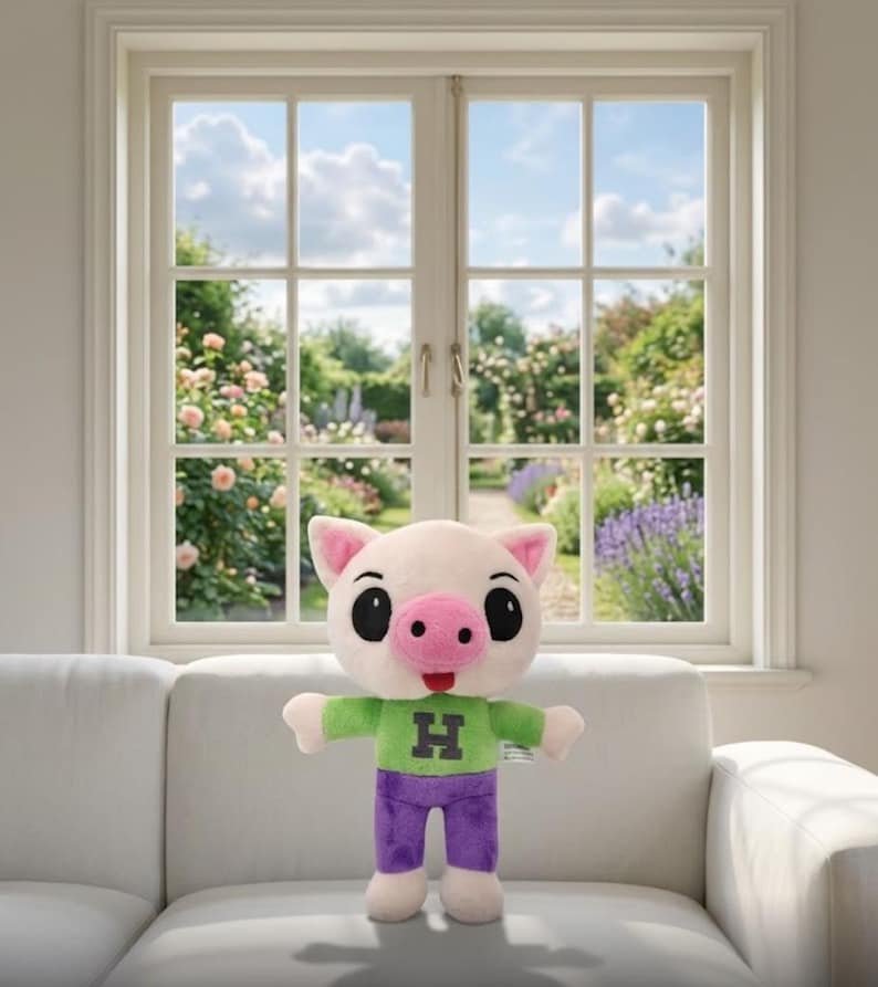 Op de afbeelding: Een pluchen varken met een lichtroze gezicht, oren en snuit, en grote zwarte ogen. Het draagt een groen shirt met een zwarte "H" en een paarse broek. Het speelgoed staat op een witte bank.