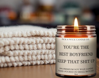 Peut inclure: Une bougie allumée dans un bocal en verre avec l'inscription "YOU'RE THE BEST BOYFRIEND KEEP THAT SHIT UP". La bougie est de 227g et faite de cire de soja. Une pile de tissu tricoté crème est à gauche.