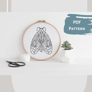 May include: A black and white line drawing of a moth with intricate details, displayed in a wooden embroidery hoop on a white surface. The text "PDF PATTERN" is visible in the upper right corner of the image.