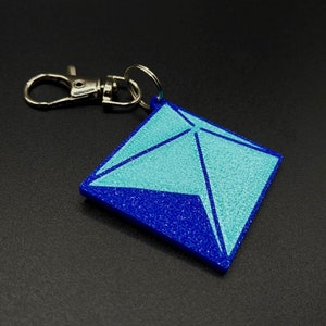 May include: A blue and turquoise geometric keychain with a silver split ring.