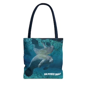 May include: A tote bag with a navy blue handle and a vibrant image of a manatee swimming underwater. The manatee is gray and white, set against a blue background. The text "SEA POTATO ENERGY" is printed in white.