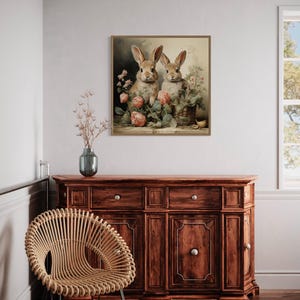 a cozy corner of a room with a wooden dresser, a woven chair, and a framed painting of two rabbits sitting together.