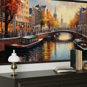 a large painting of a canal scene with boats and buildings, hanging on a wall above a wooden table with a lamp and some books.