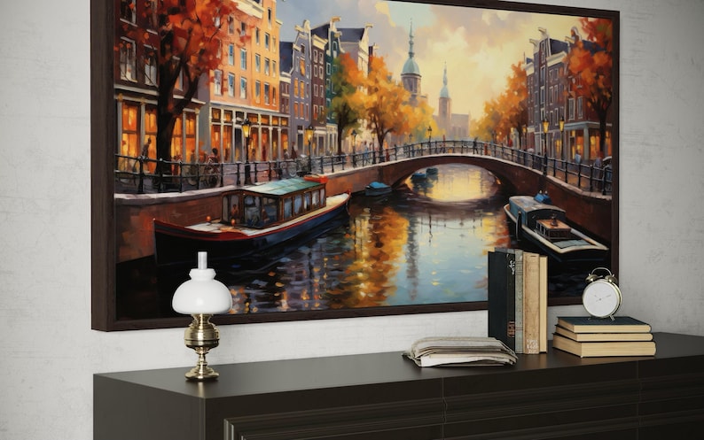 a large painting of a canal scene with boats and buildings, hanging on a wall above a wooden table with a lamp and some books.