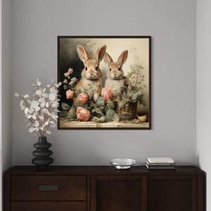 a framed painting of two rabbits sitting in a vase filled with flowers, placed on a wooden dresser in a living room setting.
