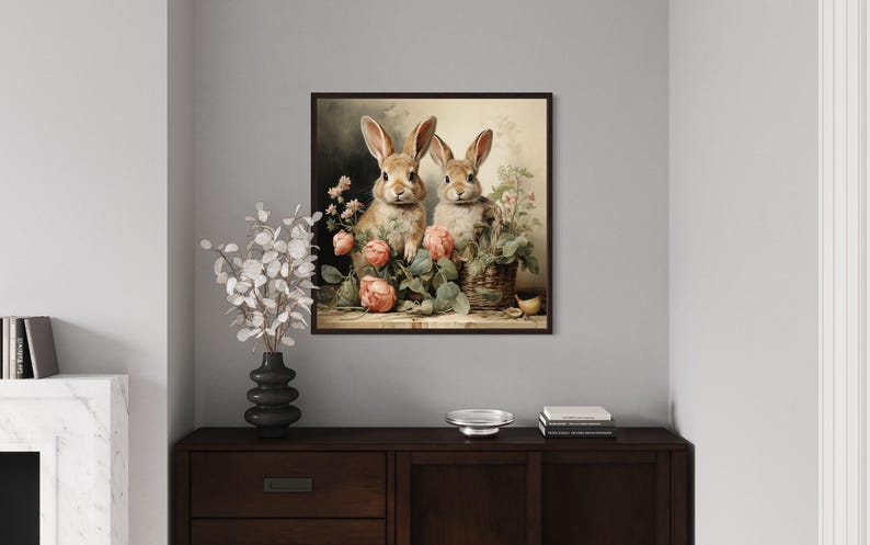 a framed painting of two rabbits sitting in a vase filled with flowers, placed on a wooden dresser in a living room setting.