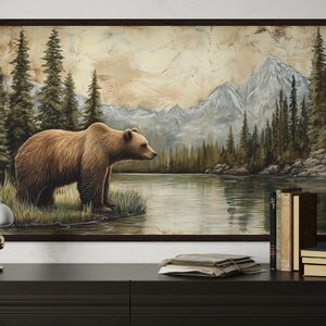a large painting of a bear standing on a grassy bank by a lake, with mountains in the background.