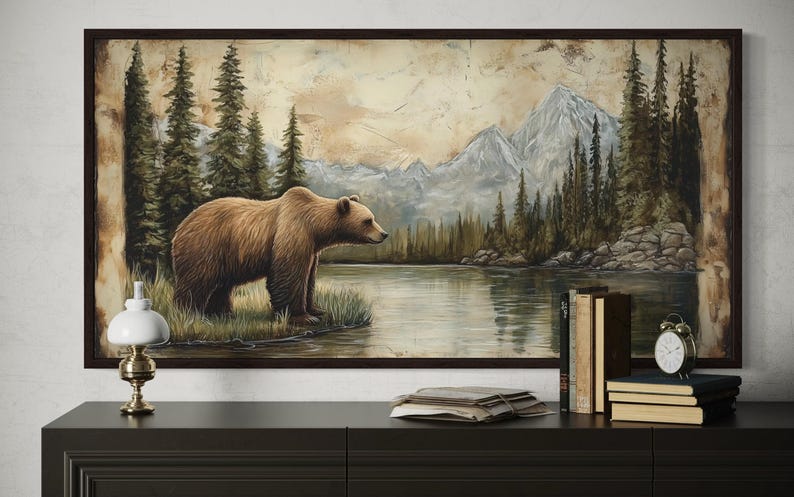 a large painting of a bear standing on a grassy bank by a lake, with mountains in the background.
