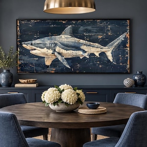 May include: A large rectangular wall art piece featuring a detailed painting of a shark swimming against a dark, distressed wooden plank background, framed in a thin black border and displayed above a dark blue sideboard in a dining room.