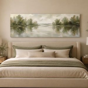 Pode incluir: Uma pintura de paisagem retangular e larga apresentando um lago calmo cercado por árvores verde-suaves sob um céu nublado. A obra de arte é exibida acima de uma cama estofada bege com almofadas combinando e uma manta verde num quarto.