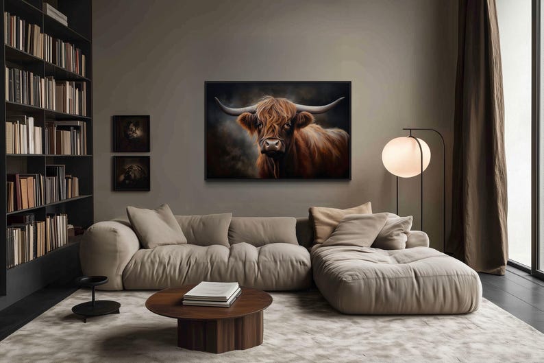a cozy living room with a large, comfortable couch and a coffee table. Above the couch, there is a framed painting of a cow with long horns, adding a unique touch to the room's decor. The room also features a bookshelf filled with books, creating a warm and inviting atmosphere.