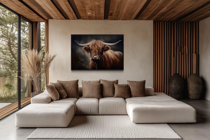 a large, white sectional sofa with brown throw pillows, positioned in front of a large window that offers a view of trees. Above the sofa, there is a framed painting of a cow with horns.