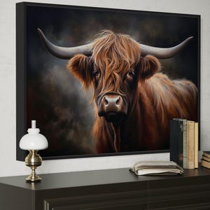 a large framed painting of a brown cow with long horns, displayed on a wall above a wooden dresser.