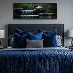 a serene bedroom scene with a large bed adorned with blue and gray bedding, flanked by two nightstands with lamps. Above the bed, a framed picture of a waterfall and flowers adds a touch of nature to the room's decor.
