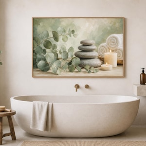 May include: A rectangular wall art print featuring a stack of smooth grey stones, green eucalyptus branches, two lit cream-coloured candles, and rolled white towels against a soft, muted green and beige background, displayed in a wooden frame.