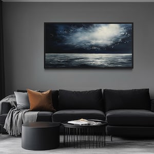 a modern living room with a large black sectional sofa, a round black coffee table, and a framed painting of a seascape hanging on the wall above the sofa.