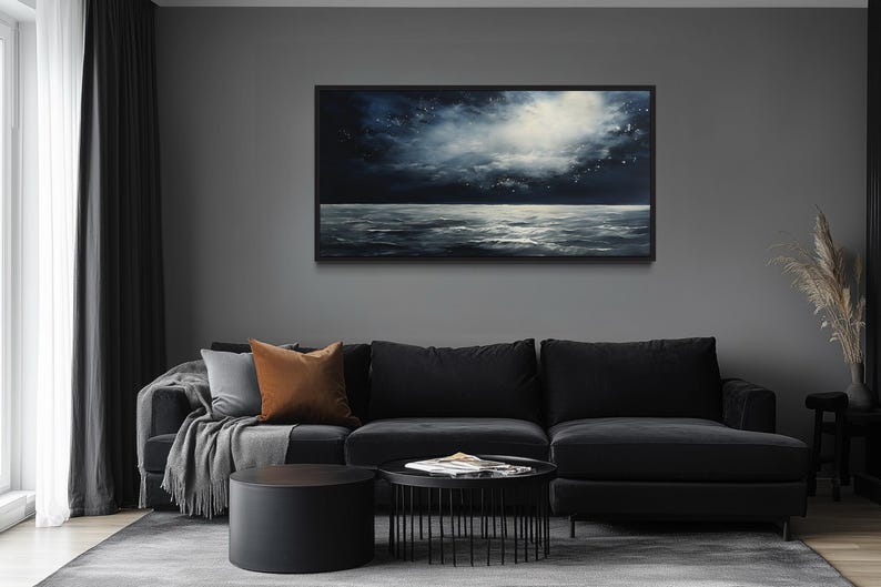 a modern living room with a large black sectional sofa, a round black coffee table, and a framed painting of a seascape hanging on the wall above the sofa.