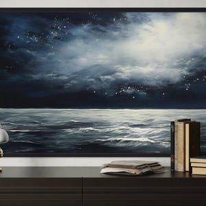a large painting of a night sky with a dark blue background and white stars, hanging on a wall above a wooden dresser. On the dresser, there is a lamp, a stack of books, and a clock.